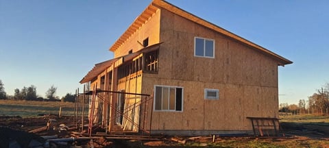 A house under construction with wooden framing and exterior sheathing in an open field