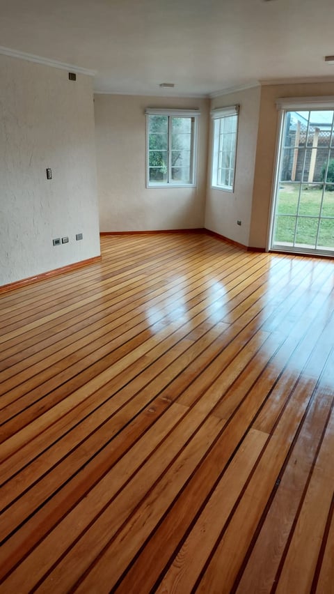 Empty living room with polished wooden floor, white walls, windows, and glass patio door overlooking garden