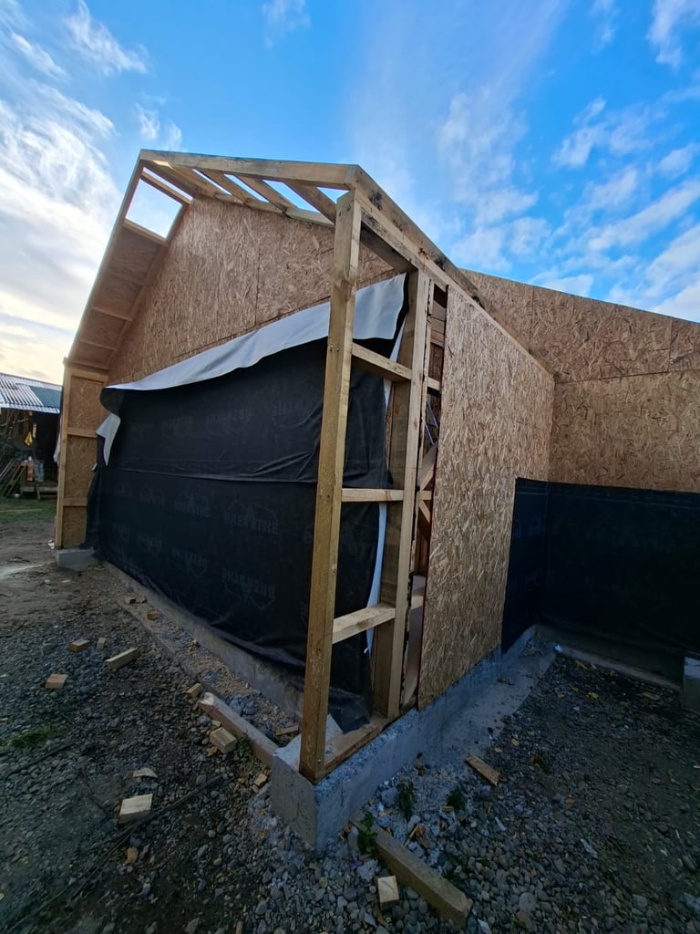 Rustic wooden structure with cork insulation, black tarp, and wooden frame under construction against blue sky