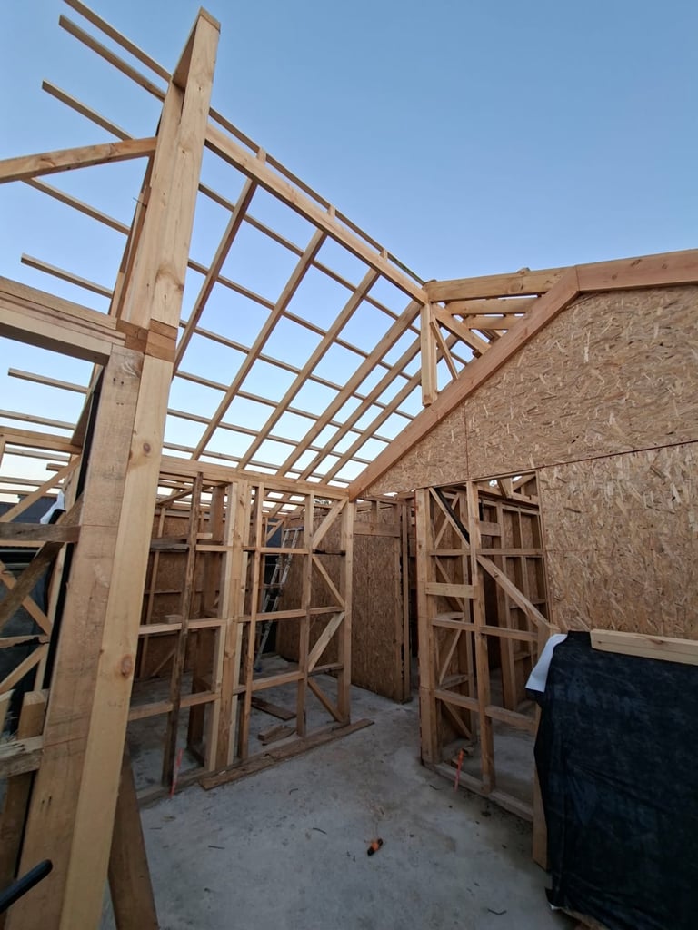Wooden framed house under construction with exposed roof trusses and OSB sheathing on walls against clear blue sky
