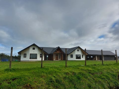 Modern house with white and dark wood exterior surrounded by green pasture and wooden fence under cloudy sky