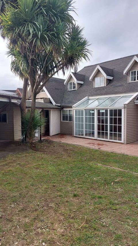 Suburban house with gray roof, white trim, brick patio, glass sunroom addition, and palm tree in front yard