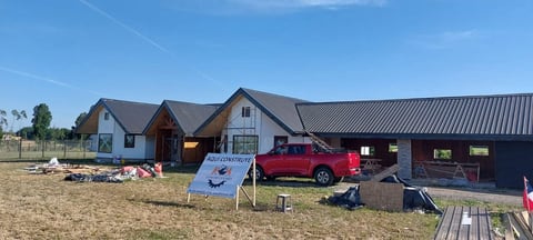 Modern farmhouse with metal roof and red pickup truck parked outside, construction materials and equipment visible in the yard