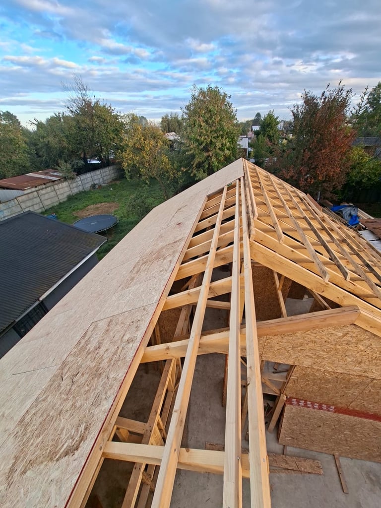 Wooden roof framing under construction with exposed rafters and plywood sheathing on a residential house